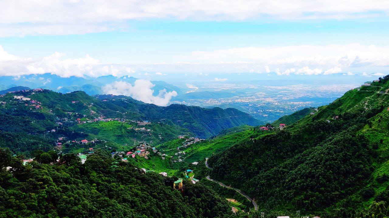 Panoramic view of Dehradun valley with lush green hills, winding mountain roads, and distant city landscape in Uttarakhand