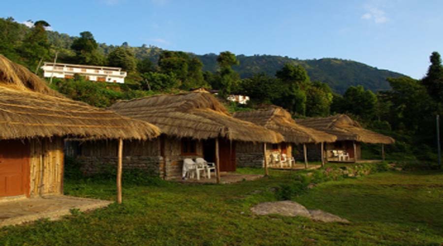 Traditional Kumaoni village cottages with thatched roofs in Uttarakhand, surrounded by green hills and forest, showcasing rural heritage stays and peaceful Himalayan countryside experience.