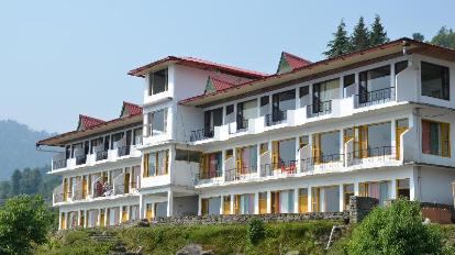 Mountain-view hillside hotel building with multiple balconies, white exterior walls, red sloped roofs, and large windows overlooking greenery and forested surroundings.